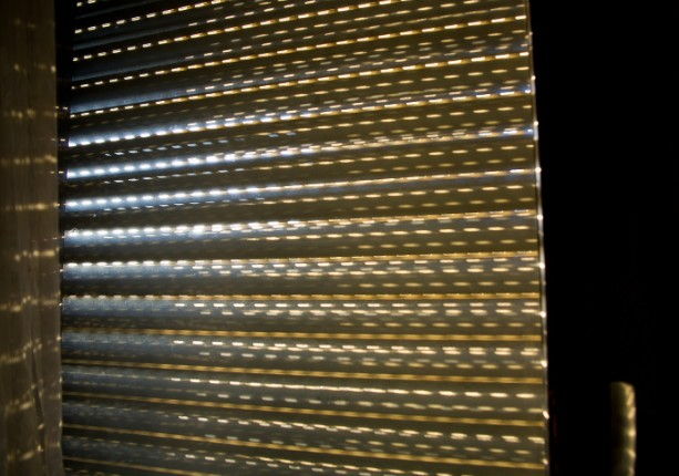 Persiana de seguridad de lama microperforada a contraluz, con la luz exterior pasando por las perforaciones