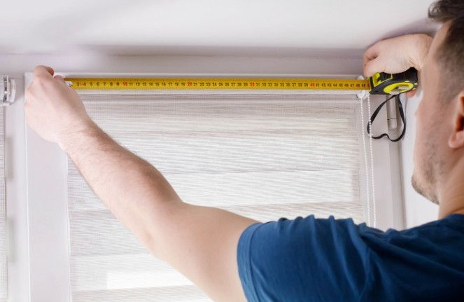 Técnico comprobando con flexómetro el ancho de un estor enrollable a medida ya montado en la ventana