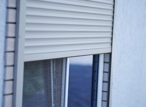Persiana blanca a media ventana con una mosquitera fija montada detrás, en una vivienda de Burgos