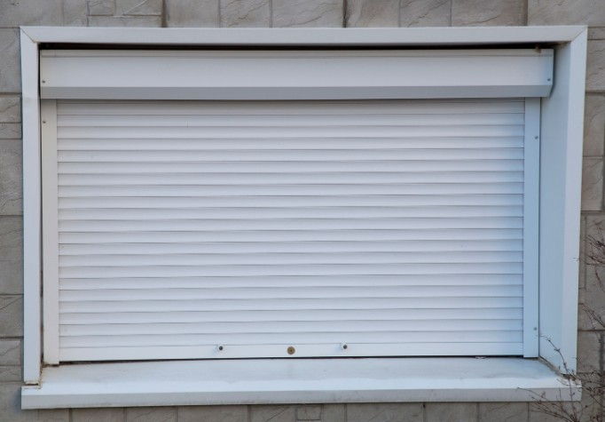 Persiana de PVC blanca bajada del todo en una ventana con cajón exterior y vierteaguas de piedra