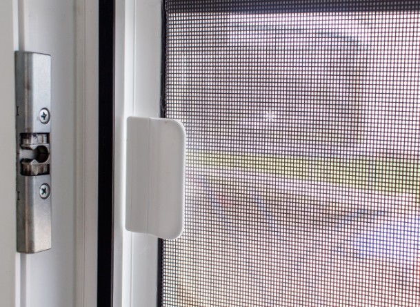 Tirador blanco de una mosquitera corredera junto al cerradero metálico de la ventana
